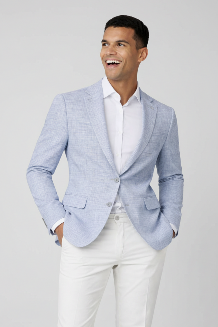 Colbert miniruit lichtblauw worn by a smiling man in a stylish outfit with white trousers.