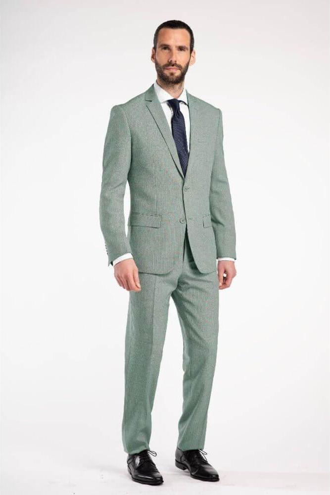 Man in pak pinstripe groen 3-delig suit, standing confidently with a tie and dress shoes.