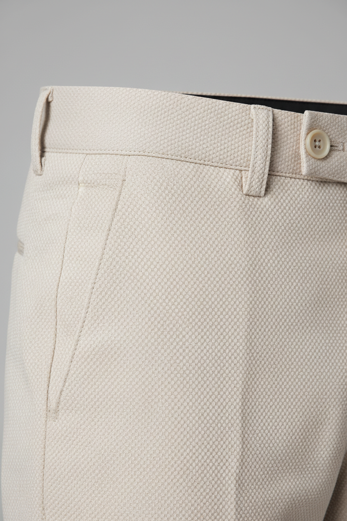 Pantalon stretch pique zand close-up showing fabric texture and button detail.