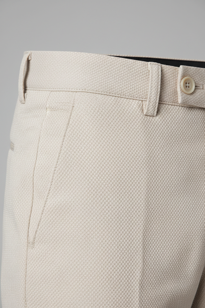 Pantalon stretch pique zand close-up showing fabric texture and button detail.